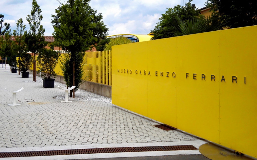 Enzo Ferrari House Museum entrance with yellow wall and trees in Modena, Italy.