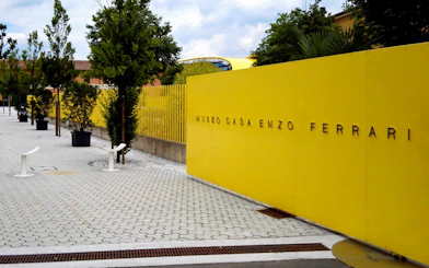 Enzo Ferrari House Museum entrance with yellow wall and trees in Modena, Italy.