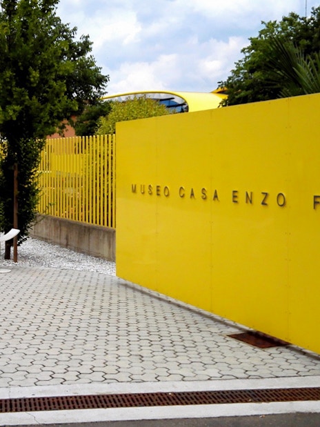 Enzo Ferrari House Museum entrance with yellow wall and trees in Modena, Italy.