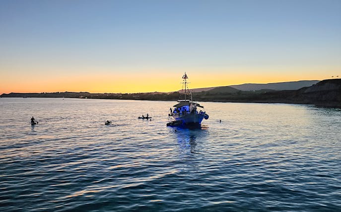 Boat on sunset cruise in Kefalonia with people swimming nearby.