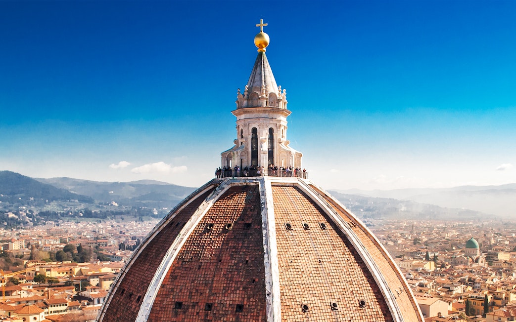 Florence Duomo dome with visitors on secret terraces, cityscape in background.