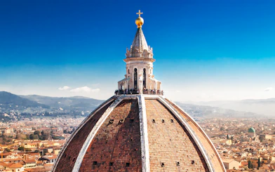 Florence Duomo dome with visitors on secret terraces, cityscape in background.