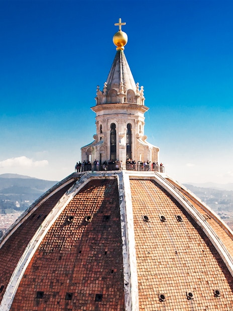 Florence Duomo dome with visitors on secret terraces, cityscape in background.