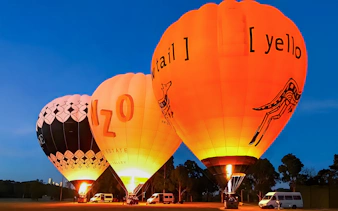 Hot air balloons illuminated at dawn, preparing for takeoff in a field.