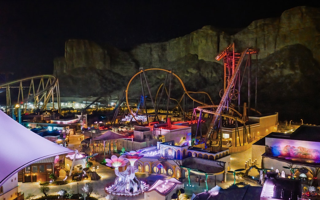 Roller coasters and attractions illuminated at night in Six Flags Qiddiya City, Saudi Arabia.