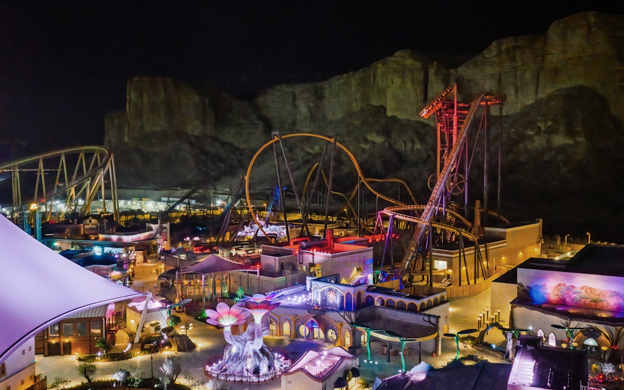 Roller coasters and attractions illuminated at night in Six Flags Qiddiya City, Saudi Arabia.