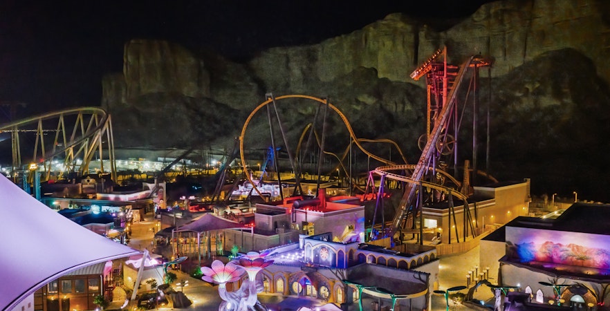Roller coasters and attractions illuminated at night in Six Flags Qiddiya City, Saudi Arabia.
