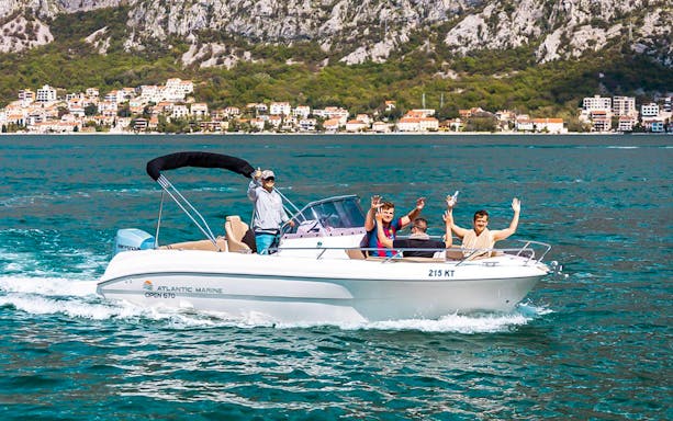 Guests waving on a speedboat during the Blue Caves tour with coastal town in the background.