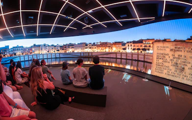 Visitors seated inside Setas de Sevilla, viewing a nighttime cityscape projection, Spain.