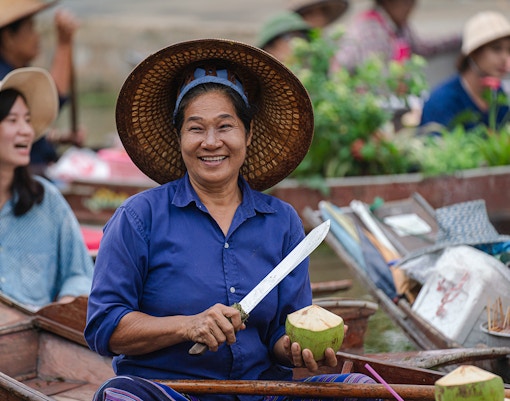 Middle age woman selling coconuts at Tha Kha floating market