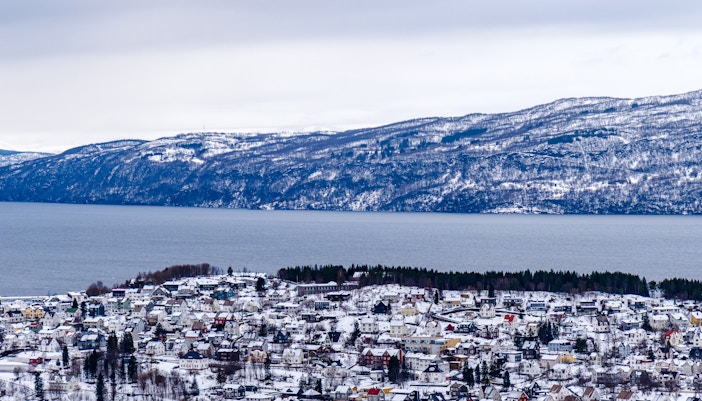 Panoramic winter view of Narvik with snowy fjord and mountains in the background.