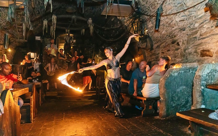 Fire dancer performing at a medieval-themed dinner with an audience in a stone-walled venue.