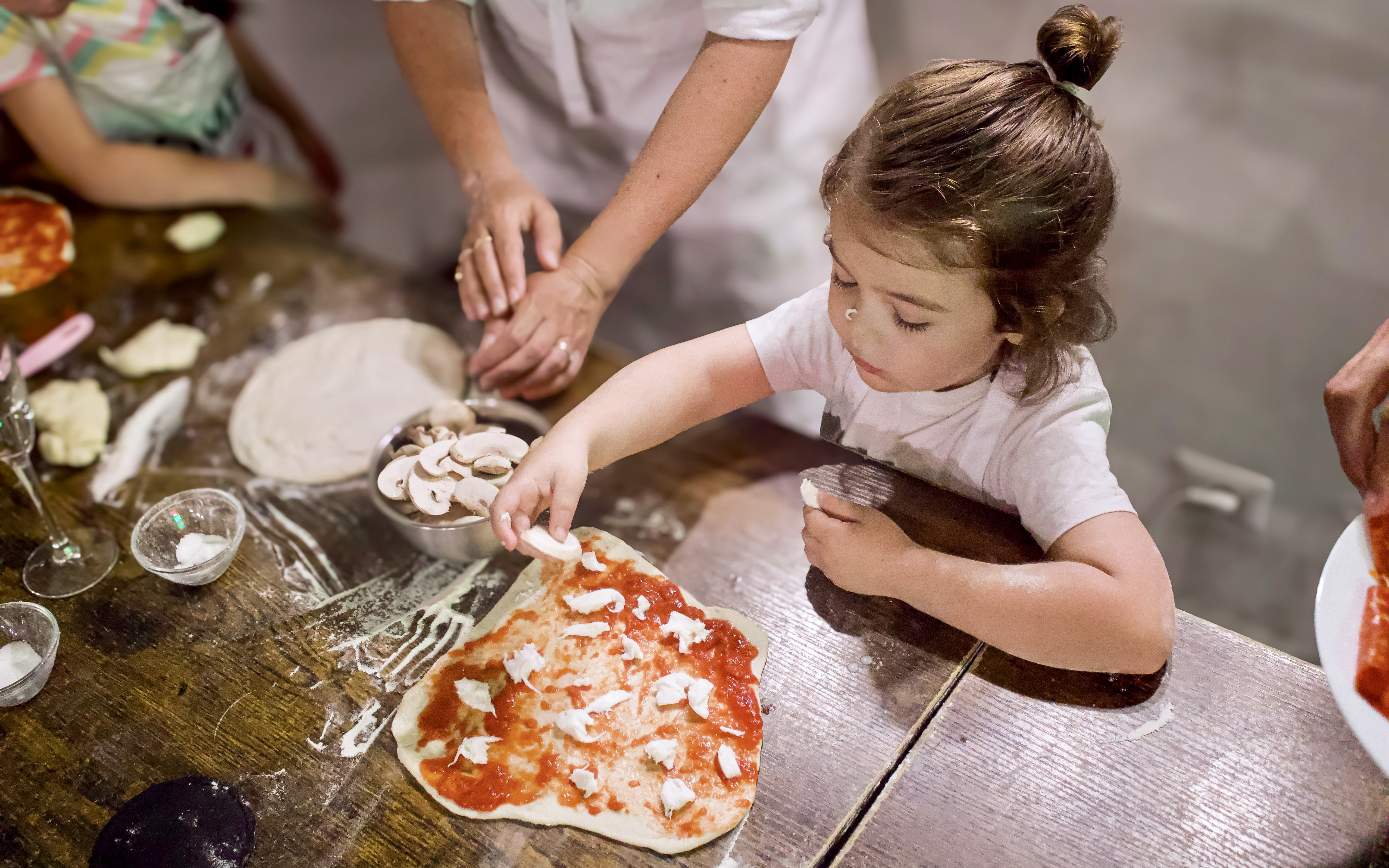 Child making pizza during Rome cooking class with dough and toppings.