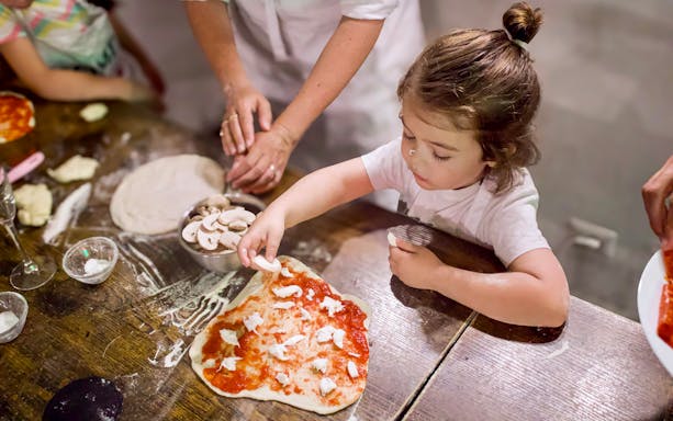 Child making pizza during Rome cooking class with dough and toppings.