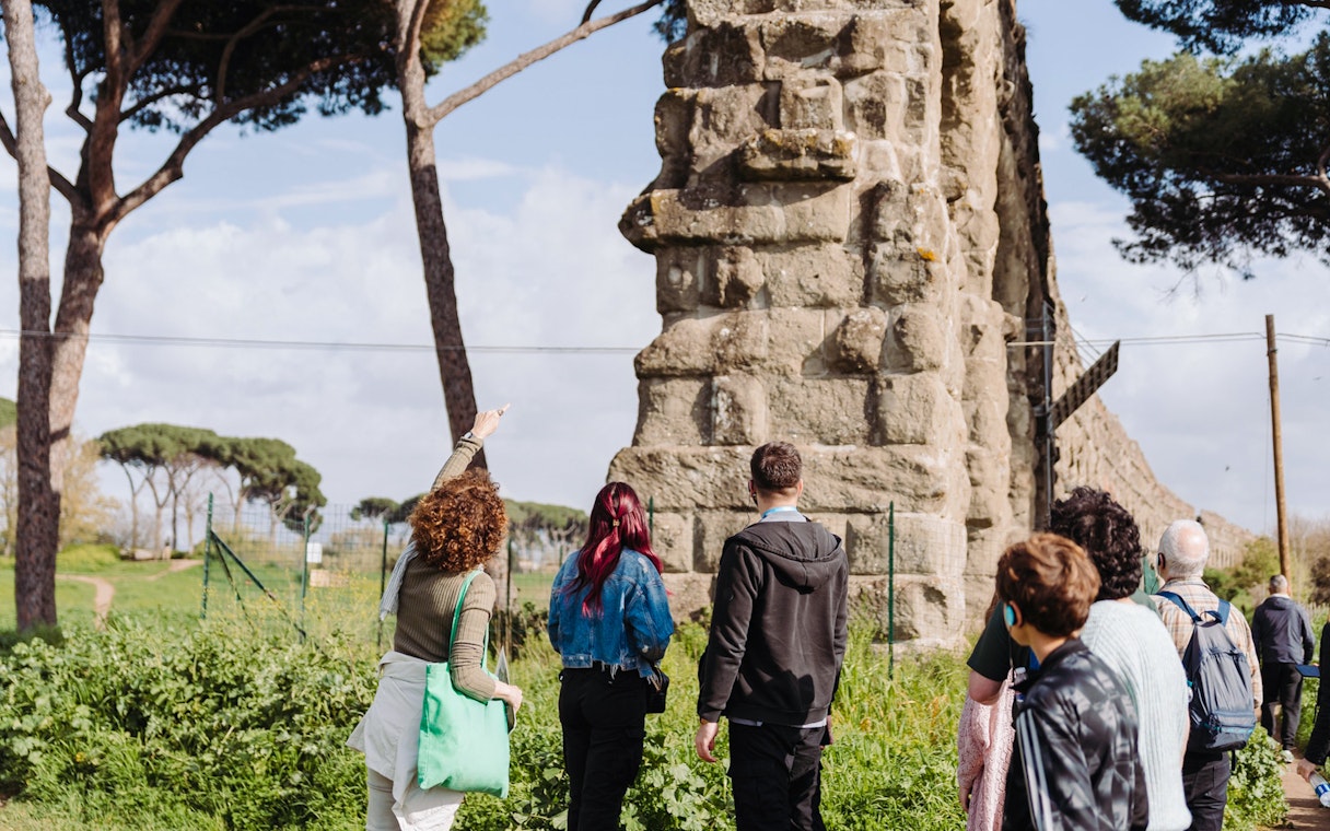 Tour group exploring ancient Roman aqueducts on the Appian Way in Rome.
