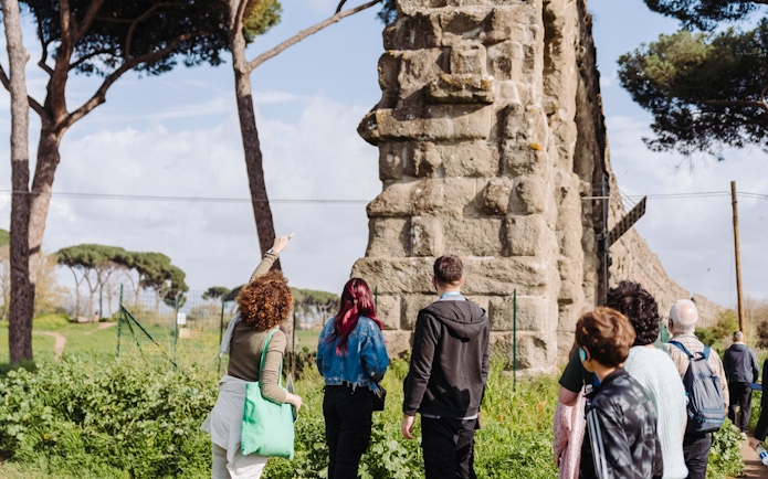 Tour group exploring ancient Roman aqueducts on the Appian Way in Rome.