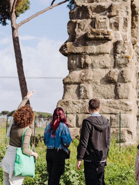 Tour group exploring ancient Roman aqueducts on the Appian Way in Rome.