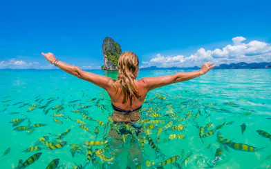 Person swimming with fish near Hong Island, Krabi, with limestone cliff in background.
