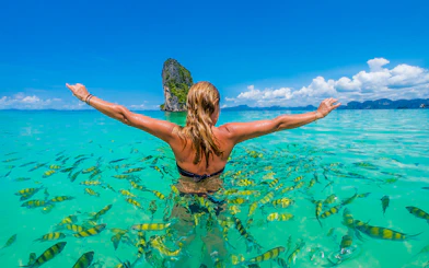 Person swimming with fish near Hong Island, Krabi, with limestone cliff in background.