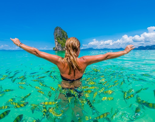 Person swimming with fish near Hong Island, Krabi, with limestone cliff in background.