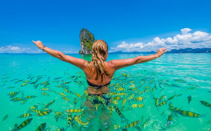 Person swimming with fish near Hong Island, Krabi, with limestone cliff in background.