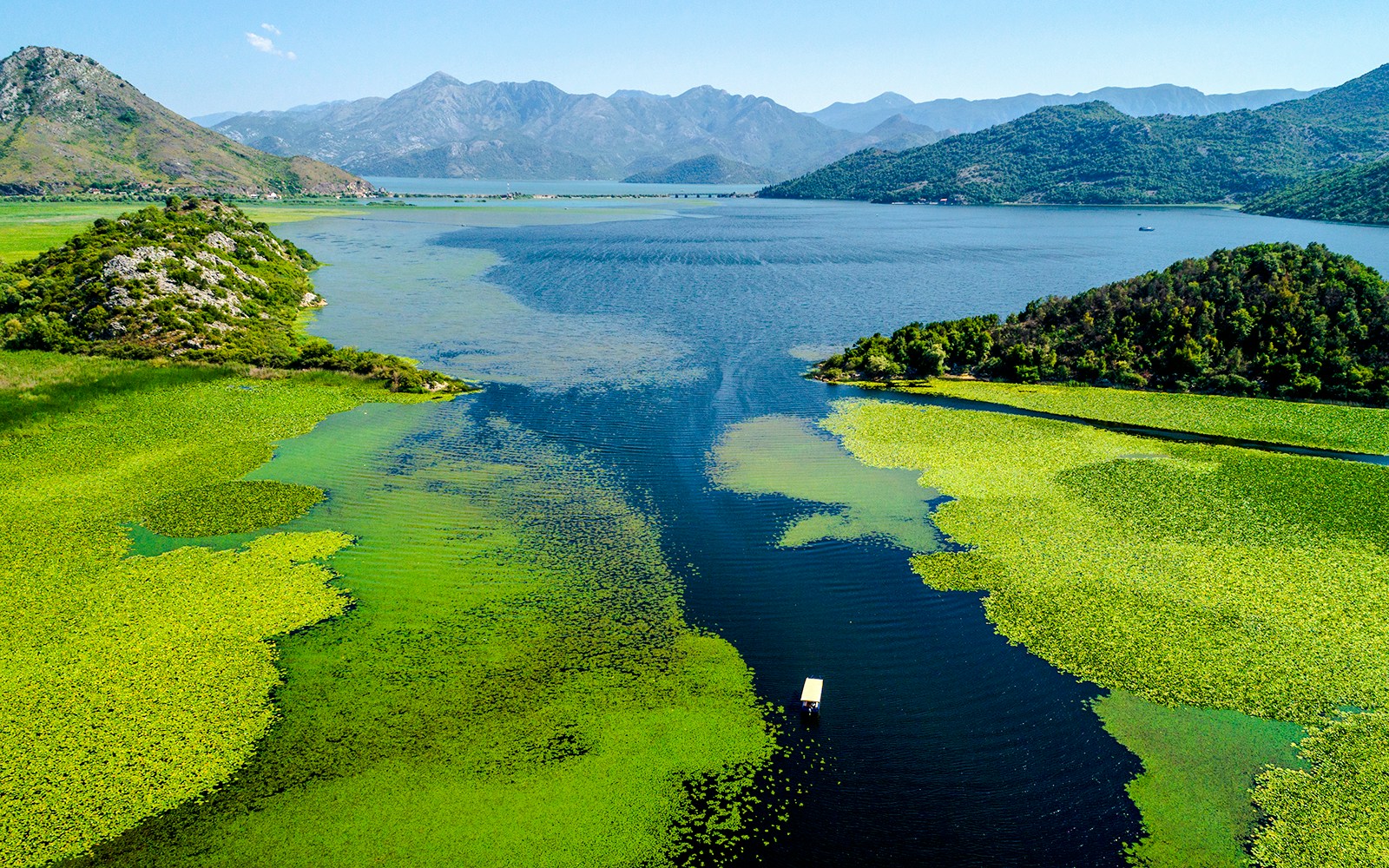 Aerial view of Lake Skadar with lush green islands and distant mountains.