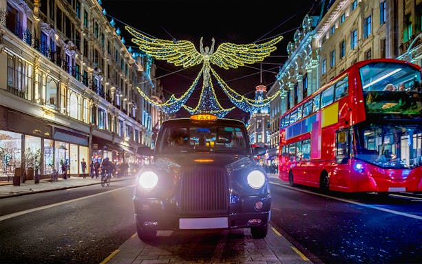 Red double-decker bus and black cab under Christmas lights on Regent Street, London.