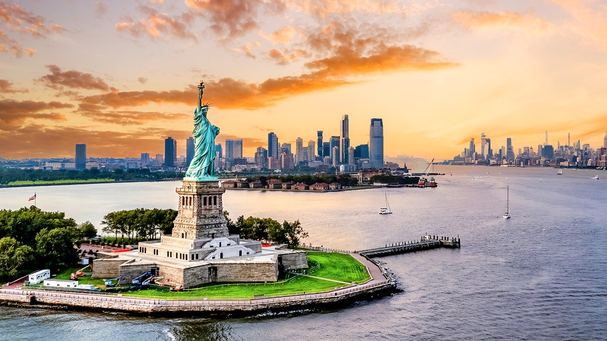 Statue of Liberty with New York City skyline at sunset.