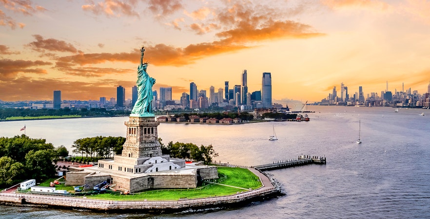 Statue of Liberty with New York City skyline at sunset.