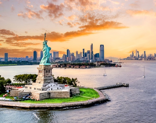 Statue of Liberty with New York City skyline at sunset.