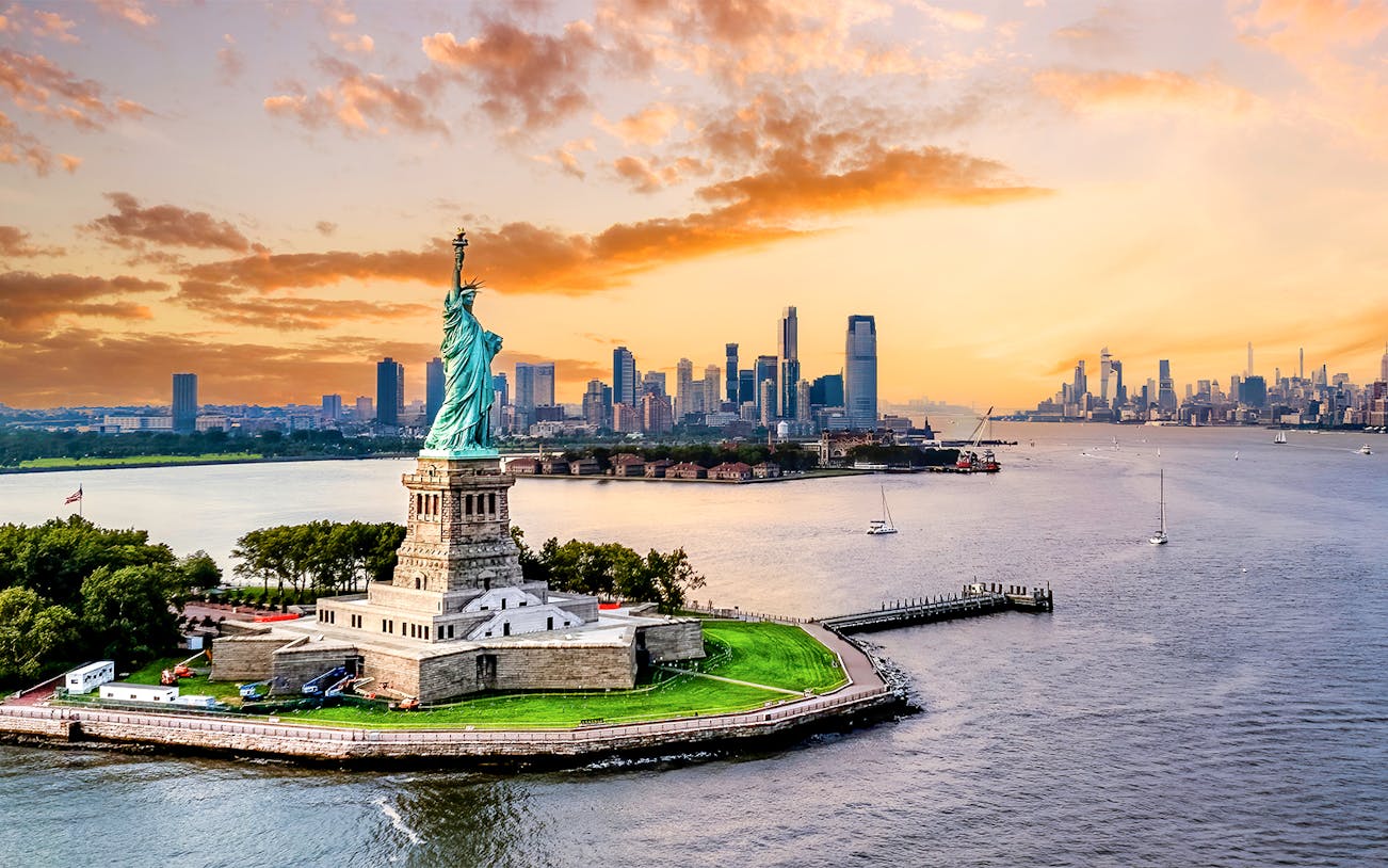 Statue of Liberty with New York City skyline at sunset.