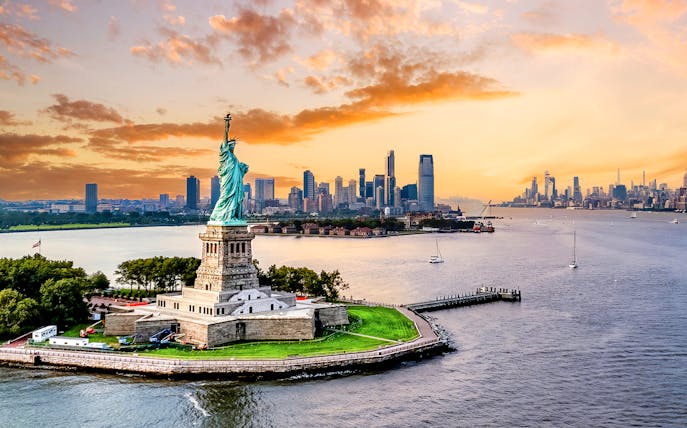 Statue of Liberty with New York City skyline at sunset.