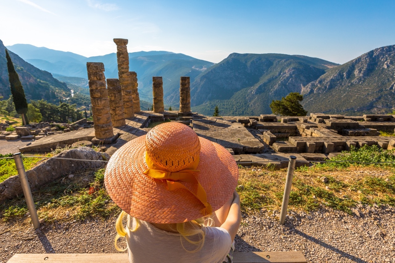 Visitor overlooking ancient ruins at Delphi, Greece, with mountains in the background.