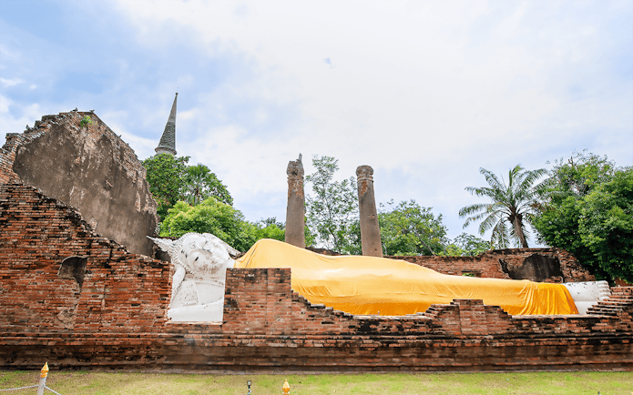 Reclining Buddha statue at Ayutthaya Temples with ancient brick ruins and trees.