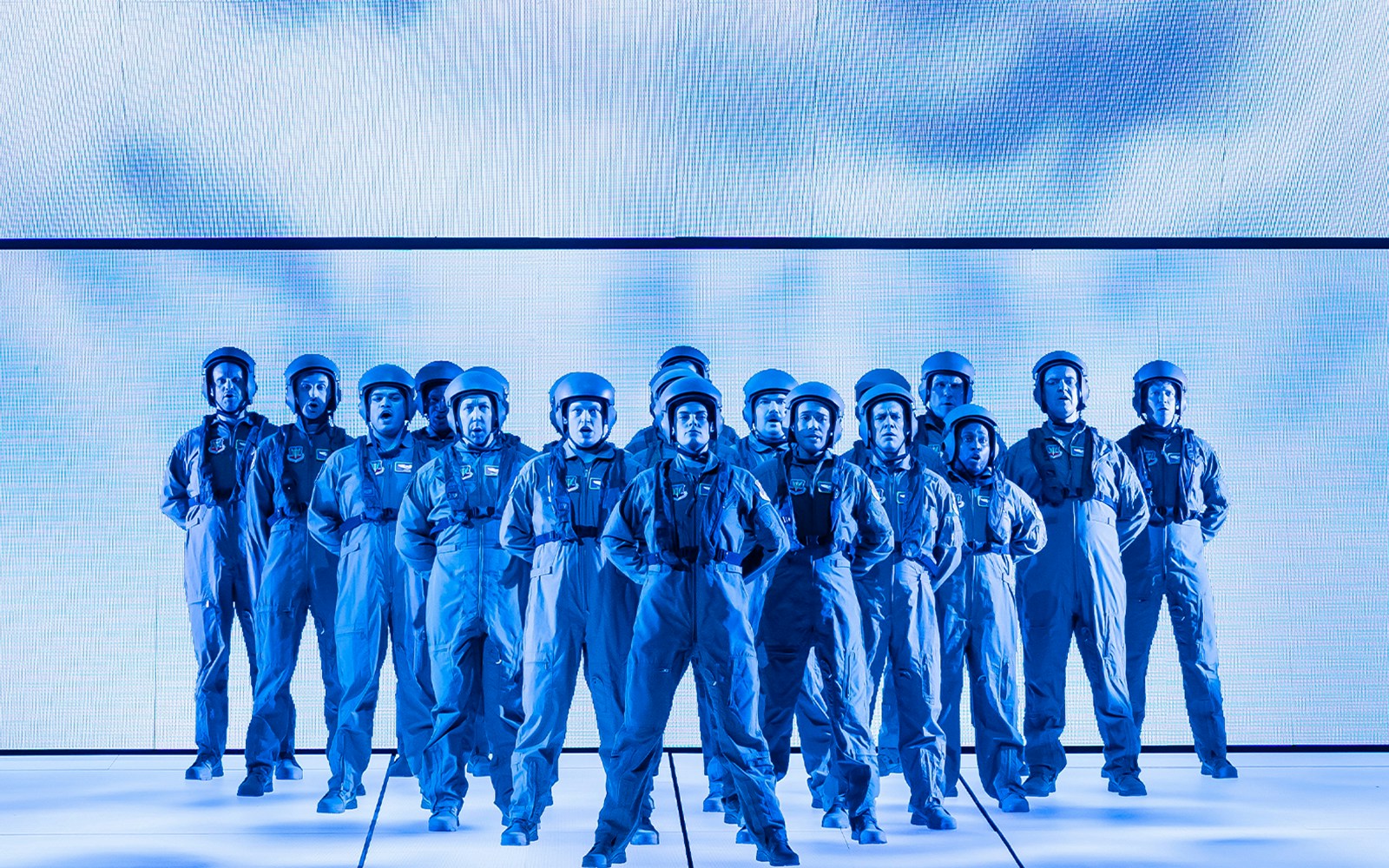 Group of people in blue jumpsuits and helmets standing in formation.