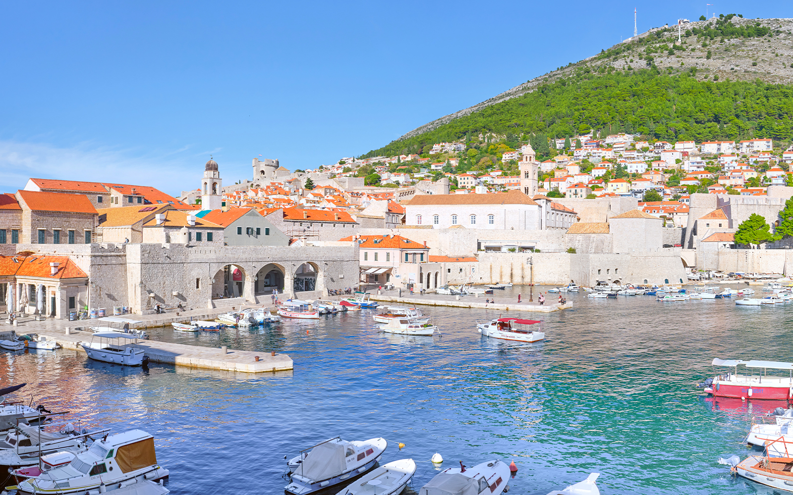 Old Port of Dubrovnik with boats and historic stone buildings under a clear sky.