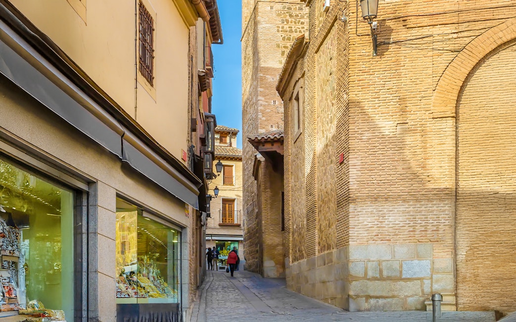 Narrow cobblestone street in Toledo with historic brick buildings and a shop window.