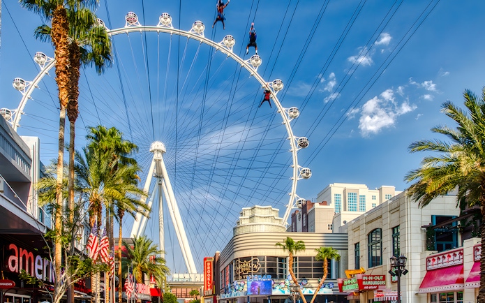 Fly LINQ Zipline riders above Las Vegas Strip with High Roller Ferris wheel in background.