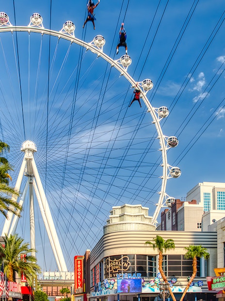 Fly LINQ Zipline riders above Las Vegas Strip with High Roller Ferris wheel in background.
