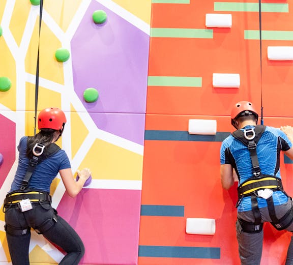 Climbers on colorful indoor rock wall at Conquer Indoor Extreme Park.