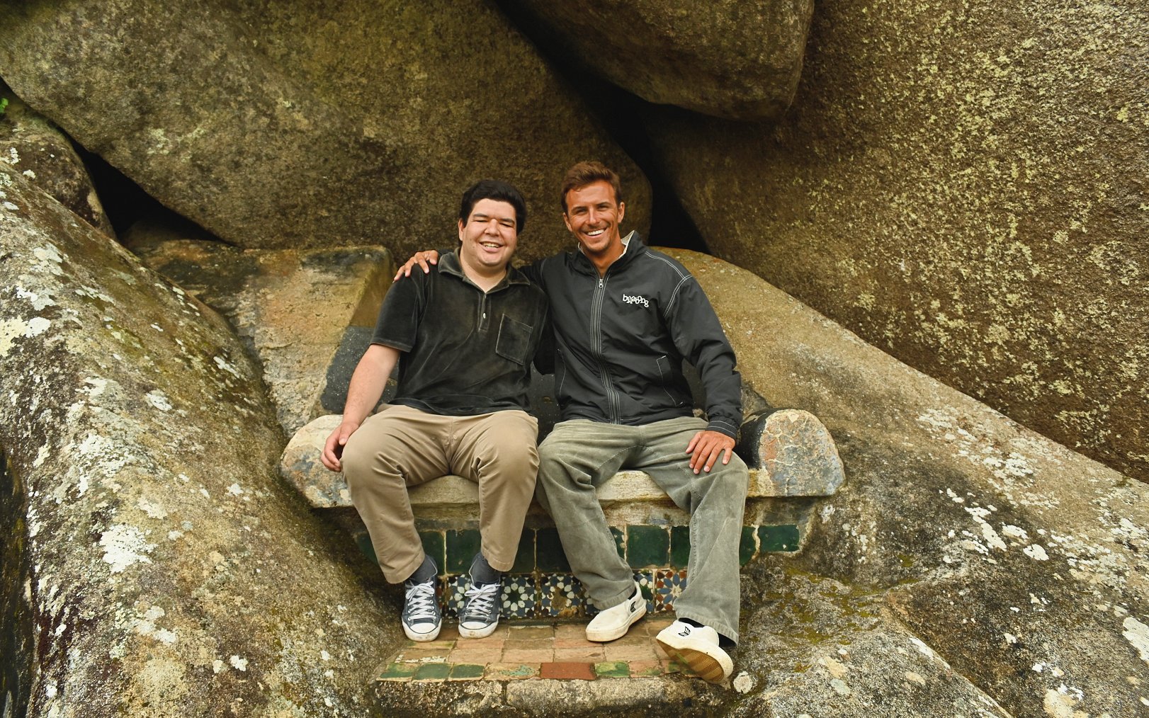 Tourists sitting on a stone bench surrounded by large rocks.