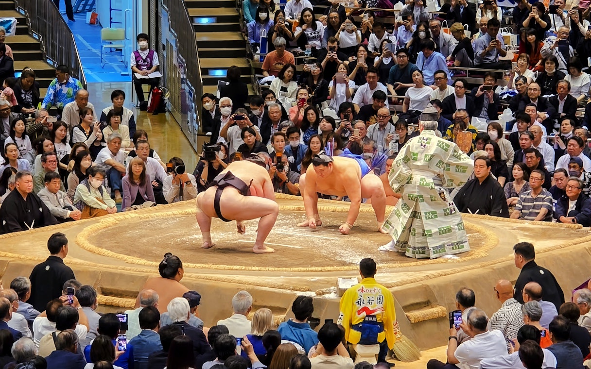 Sumo wrestlers crouching in the ring, performing pre-fight ritual in front of audience.