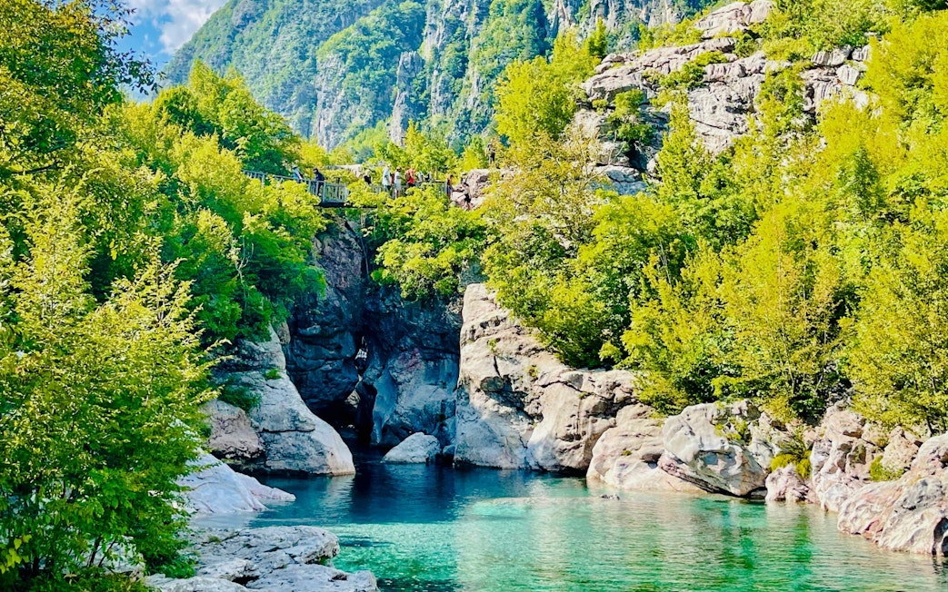 Blue Eye spring surrounded by lush greenery and rocky cliffs in Albania.