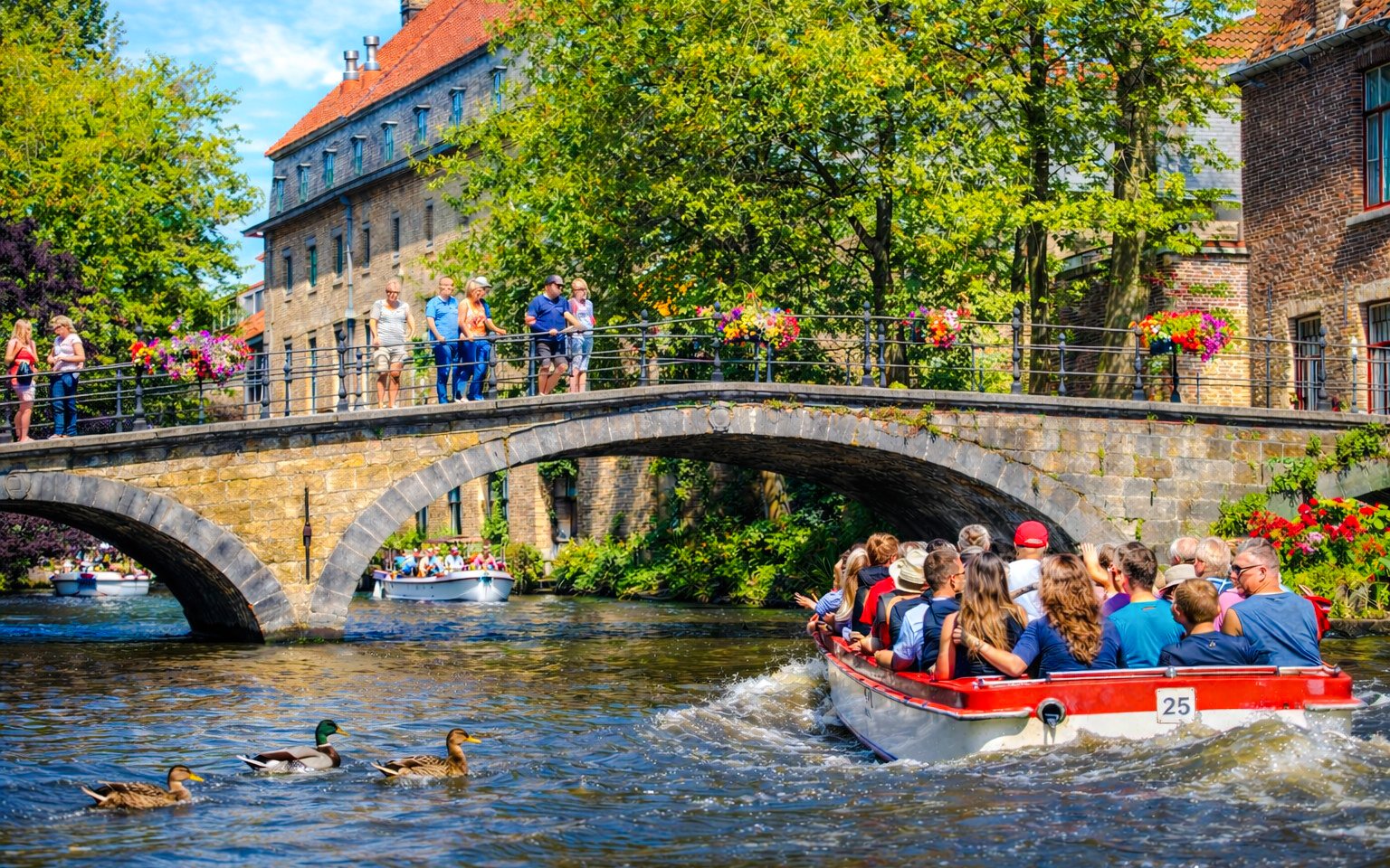 Guests on a boat ride under a stone bridge in Bruges, Belgium.