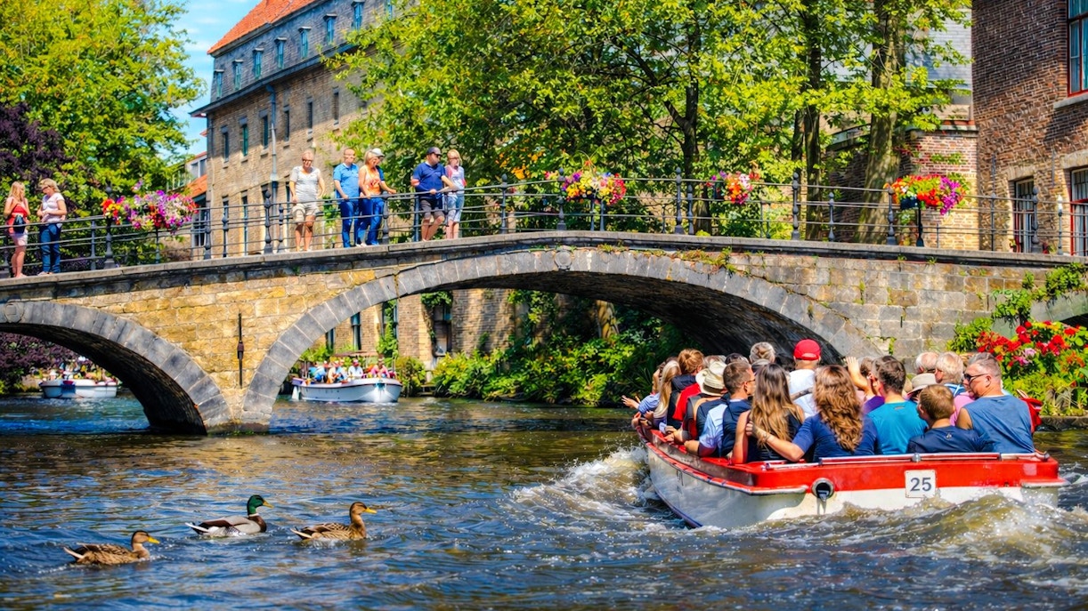 Guests on a boat ride under a stone bridge in Bruges, Belgium.