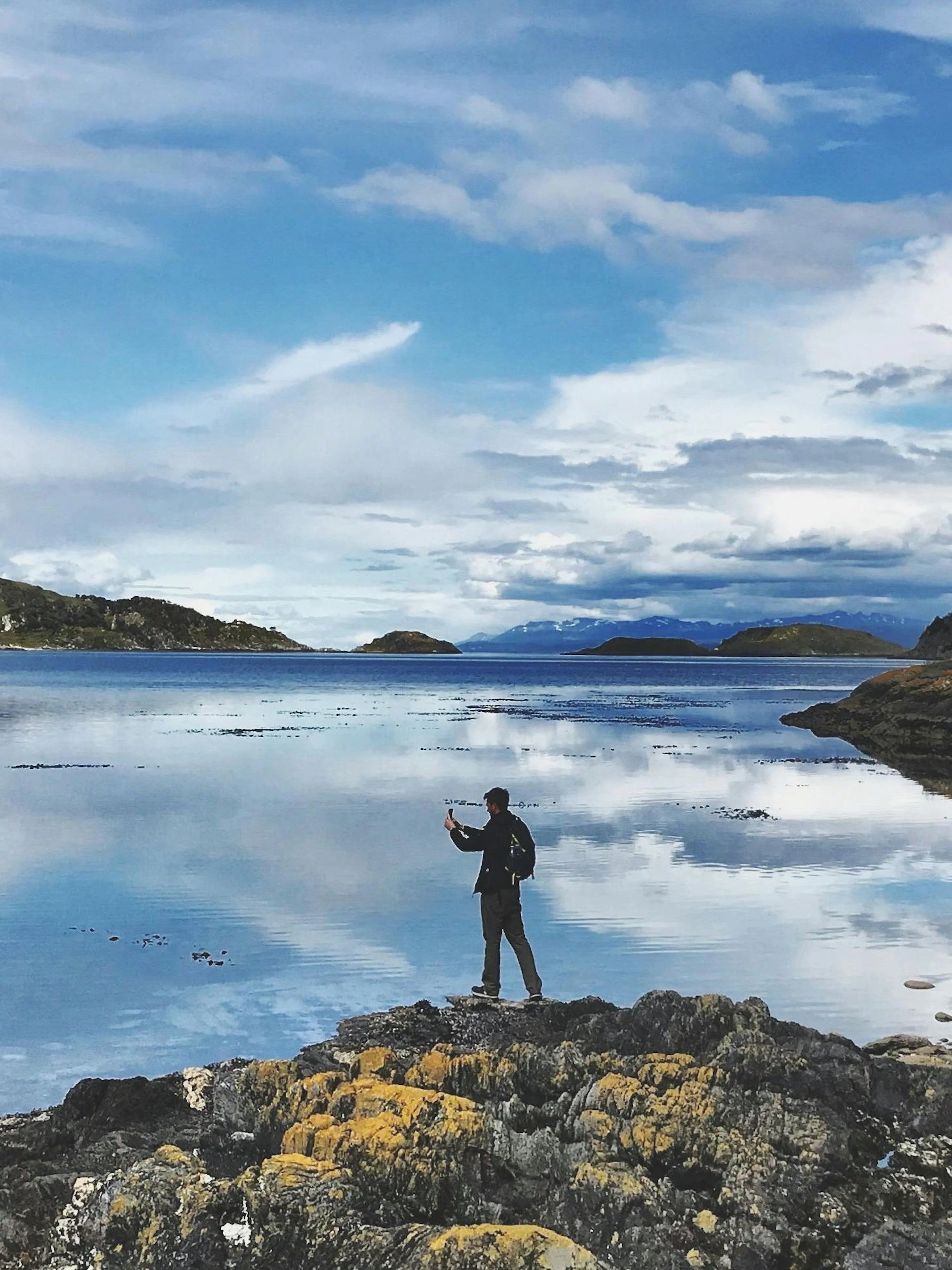 Person exploring rocky shore at Tierra del Fuego National Park with mountains in the background.