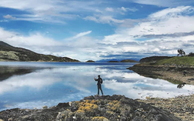 Person exploring rocky shore at Tierra del Fuego National Park with mountains in the background.