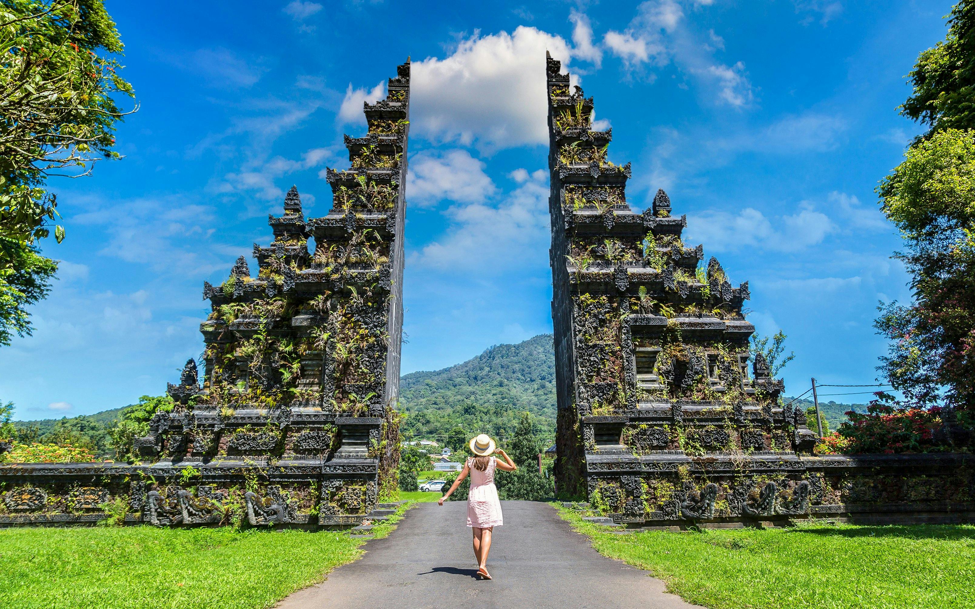 Person walking towards Bali Handara Gate with mountains in the background.
