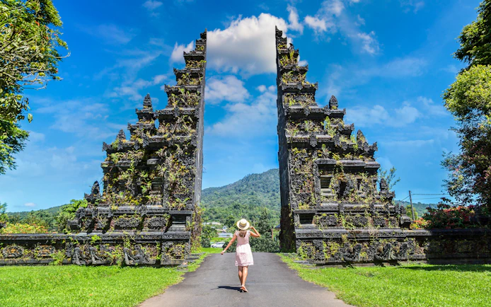 Person walking towards Bali Handara Gate with mountains in the background.