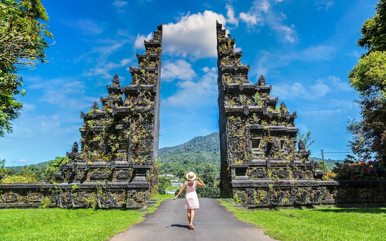 Person walking towards Bali Handara Gate with mountains in the background.